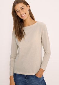 Light beige long-sleeve shirt with a rounded neckline and a smooth texture. Paired with blue denim jeans. Simple design without embellishments.