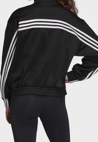 Black sports jacket featuring a high collar, elastic waistband, and white three-stripe detailing on shoulders and sleeves. Smooth texture.