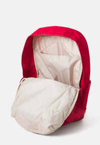 Red backpack made of durable fabric with a beige interior, featuring a spacious main compartment and mesh side pocket. Zipper closure.