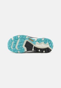 Trail running shoe sole in black, white, and turquoise. Features aggressive traction patterns, textured surface, and durable rubber materials.