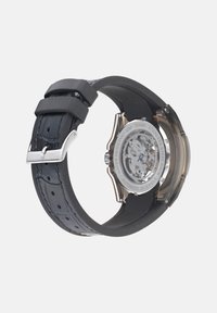 Automatikuhr mit schwarzem Gummiband und Akzenten aus Edelstahl. Transparentes Gehäuseboden offenbart das filigrane Uhrwerk. Wasserfestes Design.