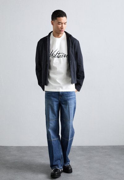 Black zip-up jacket over a white shirt with black text, paired with light blue wide-leg jeans and black platform shoes. Simple, modern design.