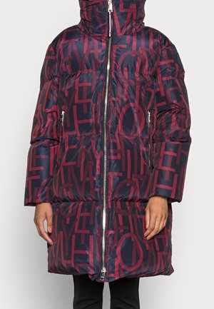 Lang navy blue puffer-jakke med rød geometrisk bogstavmønster, frontlynlås, lynlåslommer på siden og høj krave iført af en person.