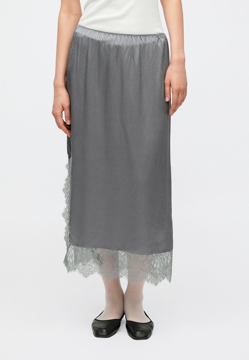 Fustă maxi gri cu talie elastică adunată, decorată cu dantelă la tiv. Textură netedă, design până la gleznă, asortată cu balerini negri.