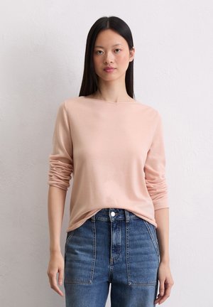 Lichtroze trui met lange mouwen en een ronde hals, gecombineerd met hoge taille blauwe denim jeans.