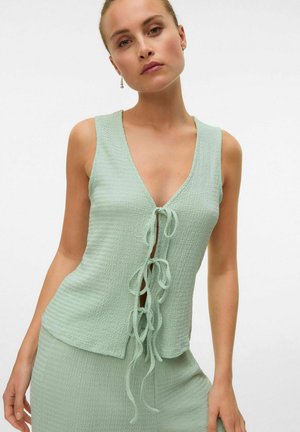 Mint green, sleeveless top with a textured fabric, V-neckline, and front tie closure. Features a relaxed fit and subtle, wavy pattern.