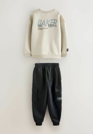 Felpa beige con testo grafico e pantaloni jogging neri con tasche cargo e logo. Tessuto morbido con vestibilità rilassata e polsini a coste.