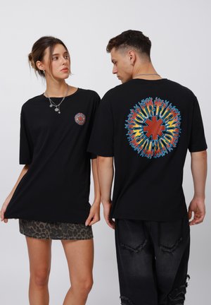 Sort oversized t-shirt med korte ærmer. Forsiden prydes af en lille farverig cirkulær grafik; bagsiden viser stor multicolor tekst og flammedesign.