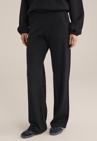 Melni, tekstūrēti bikses ar brīvu piegriezumu, ar gludu jostasvietu un nelielu izplešanos apakšā. Saskaņotas ar tumšiem dzīvokļiem.