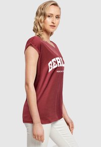 Bordeaux kortærmet t-shirt med v-hals og hvid "BERLIN" tryk. Blødt stof, afslappet pasform og en let buet nederste kant.