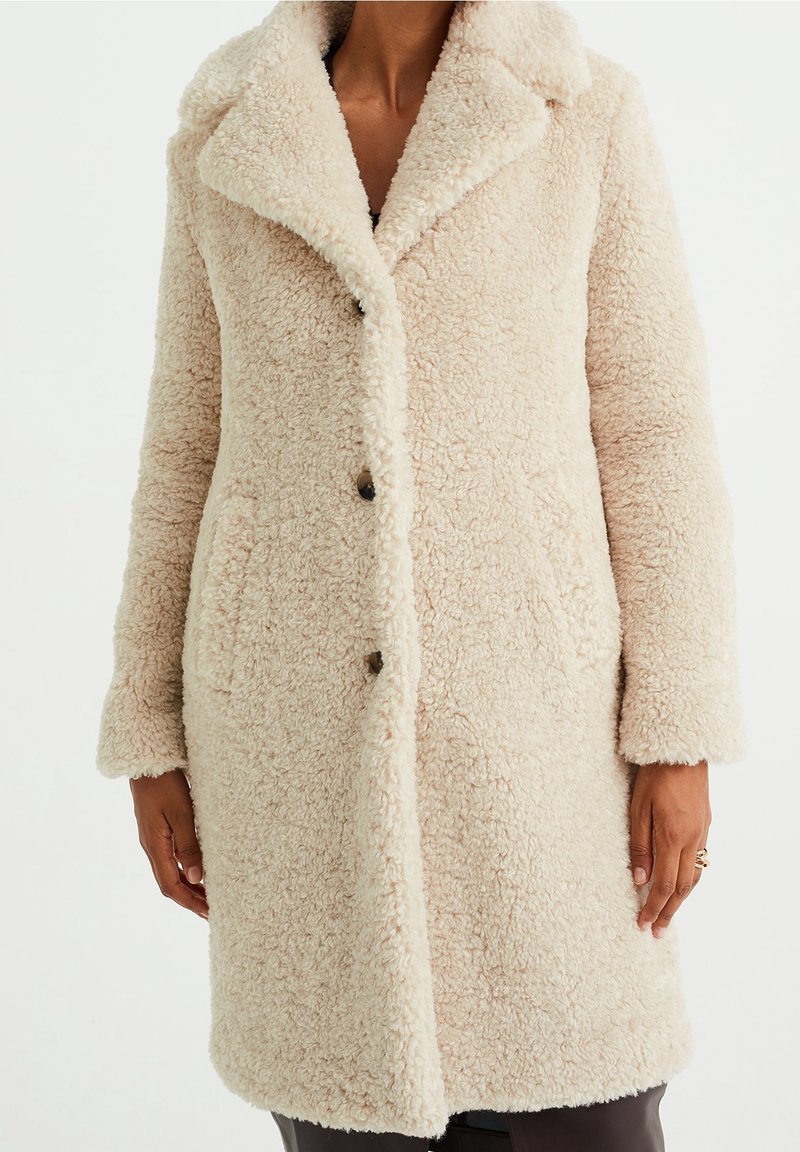 Faux pälsjacka i ljusbeige med spetsig krage, knäppningar och sidofickor. Har ett mjukt, strukturerat yttertyg.
