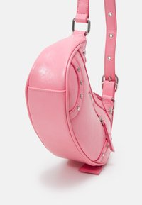 Rosa syntetisk handväska med rundad form, utrustad med silverfärgad metall, dragkedja och dekorativa nitar längs ena sidan.