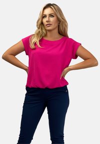 Różowa bluzka z krótkim rękawem o luźnym kroju, w połączeniu z granatowymi spodniami z zamkami błyskawicznymi. Gładka faktura i prosty design.