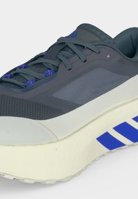 Chaussure de sport gris foncé avec des bandes bleues de la marque sur une semelle blanche, accents bleus sur les lacets et dessus en mesh respirant.