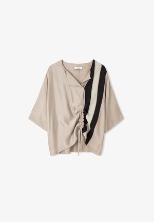Losse beige blouse met driekwart mouwen, zwarte en lichtbeige verticale strepen aan één zijde, en een gatherskoordsdetail aan de voorkant in het midden.
