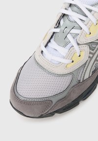 Close-up of grey and beige mesh sneaker with white laces, suede and rubber detailing, and black sole on a white background.