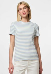 Ljusblå och krämfärgad randig t-shirt med kort ärm, ribbad struktur, rund halsringning, figurnära passform, bärs med vita byxor.