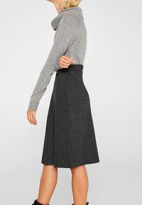 Pull en maille gris avec un col cheminée associé à une jupe noire à carreaux taille haute, avec un design évasé et une texture subtile.