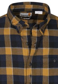 Geruite overhemdbloes met marineblauw, geel en bruin. Gemaakt van een stof met een zachte textuur. Heeft een puntkraag en een borstzak.