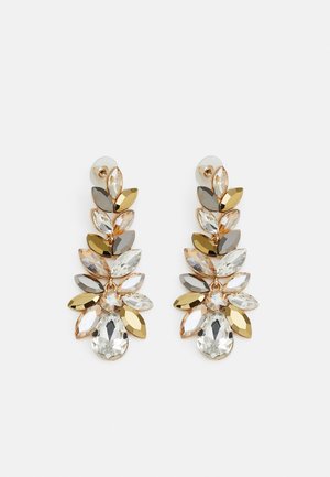 Longues boucles d'oreilles pendantes avec des cristaux en forme de feuilles dorées et argentées, disposés en motif floral sur fond blanc.