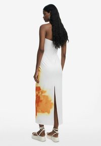 White midi dress with orange floral pattern at the hem, side slit, and a fitted design. Paired with beige strappy sandals.