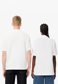 Dwaj mężczyźni w białych koszulach polo, o prostym fasonie z krótkim rękawem, w połączeniu z ciemnymi dżinsami i niebieskim denimu.