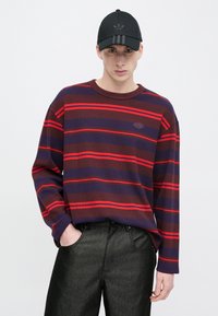 Ριγέ μακρυμάνικο πουκάμισο σε σκούρο μωβ και κόκκινο, με ανάγλυφη υφή και στρογγυλή λαιμόκοψη, συνδυασμένο με σκούρο γκρι παντελόνι.