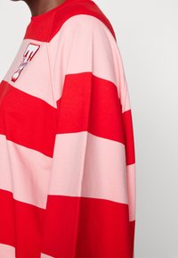 Camisa de manga larga a rayas rojas y rosas hecha de una tela suave, con cuello redondo y un pequeño detalle de logo en el frente.