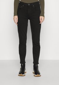 Jeans skinnies negros con cinco bolsillos, cierre de botón y cremallera. Llevados con botas de tobillo negras con suela texturizada y acentos blancos.