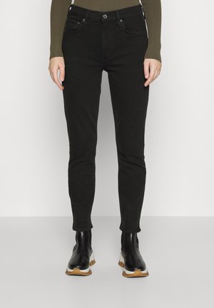 Jeans skinnies negros con cinco bolsillos, cierre de botón y cremallera. Llevados con botas de tobillo negras con suela texturizada y acentos blancos.