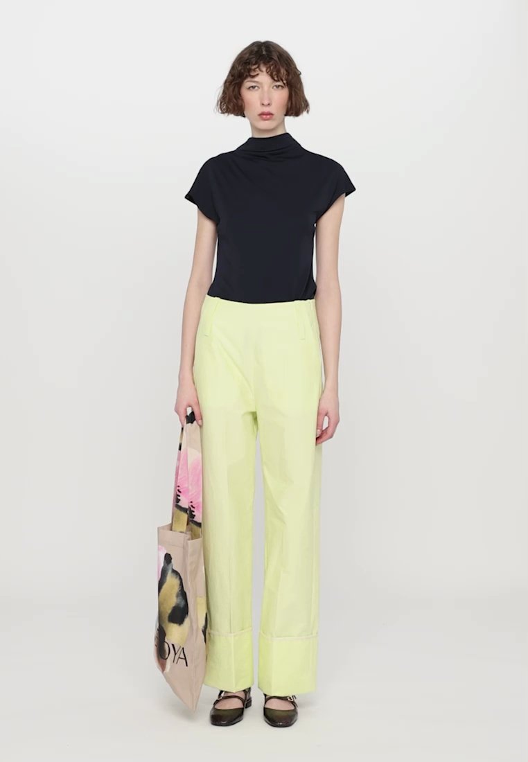 Haut à manches courtes bleu marine, col montant ; pantalon large vert citron avec détails à ourlet ; sac fourre-tout à motifs avec accents floraux ; chaussures noires.
