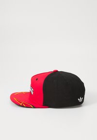 Raudona ir juoda kepurė su plokščiu kraštu, su geltonais žaibo grafika priekyje. „Adidas“ logotipas išsiuvinėtas gale.