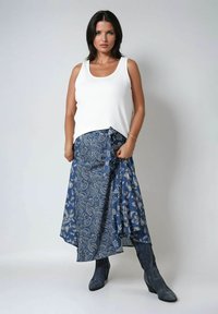 Witte geribbelde tanktop gecombineerd met een lange, blauwe rok met paisleypatroon en donkerblauwe enkellaarsjes. De rok heeft een strikdetail bij de taille.