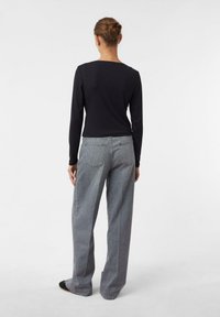Schwarzes Langarmoberteil, kombiniert mit grauen weiter geschnittenen Jeans. Die Jeans verfügen über zwei Gesäßtaschen und eine subtile Textur.
