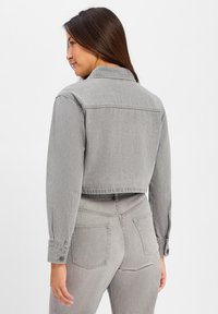 Szara dżinsowa kurtka z krótkim krojem, zapięciami na guziki i klasycznym kołnierzem. Charakteryzuje się gładką teksturą i minimalnymi detalami przeszyć.