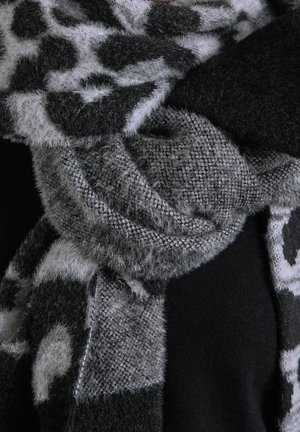 Écharpe à motifs flous noir et gris enroulée autour de vêtements noirs, montrant un tissu en tricot doux et texturé en gros plan.