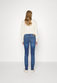 Slim-fit blue denim jeans with a mid-rise waist, five pockets, and contrasting stitching, paired with a light-colored long-sleeve top.