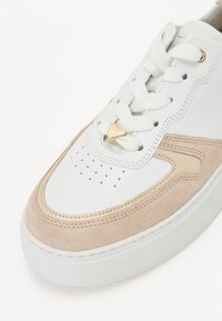 Baskets en cuir blanc avec des accents en daim beige, bout rond, œillet en forme de cœur doré et lacets blancs, avec des perforations sur le capuchon.