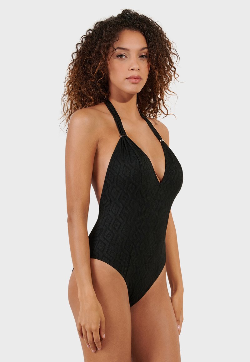 Black one-piece swimsuit with a deep V-neck, textured fabric featuring geometric patterns, halter neck design, and silver accents on straps.