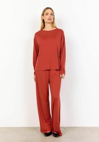 Top a maniche lunghe color ruggine e pantaloni larghi coordinati realizzati in tessuto morbido. L'ensemble presenta una vestibilità rilassata e una texture liscia, adatto per un abbigliamento casual.