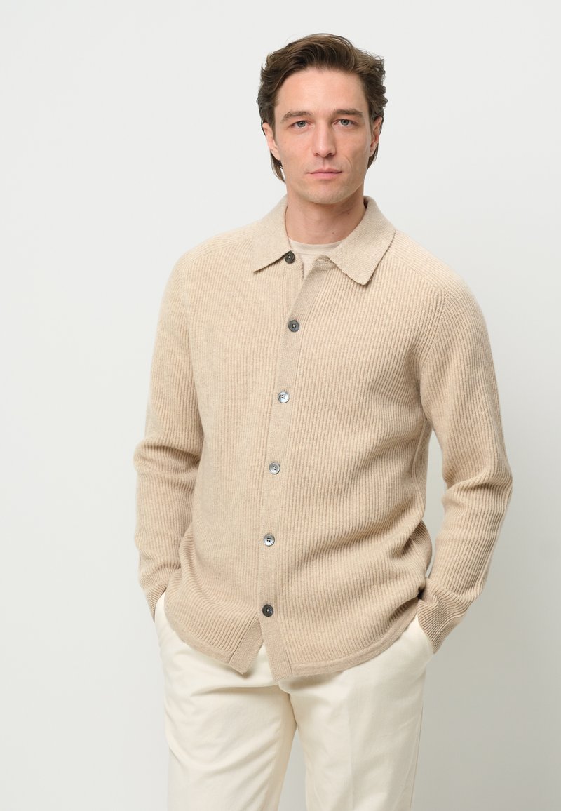 Beige ribbed cardigan with a collared neckline, front buttons, and side pockets. Textured knit fabric adds depth to the design.