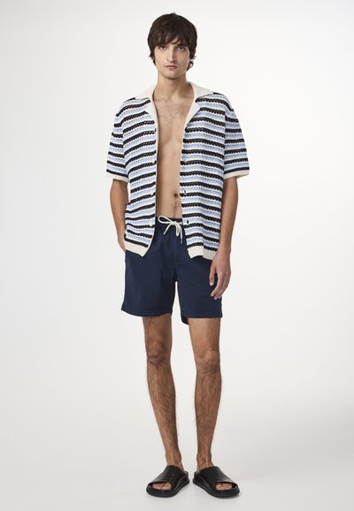 Kortärmad, randig stickad tröja i blått, vitt och svart, tillsammans med marinblå shorts. Svarta sandaler fulländar den avslappnade looken.