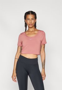 Rosa kortärmad crop top med rund halsringning och en liten vit logotyp. Kombinerad med höga svarta leggings. Slät tygtextur.