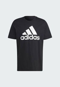 Černé bavlněné tričko s kulatým výstřihem, které má na přední straně velké bílé logo Adidas a krátké rukávy. Jednoduchý design a rovný střih.