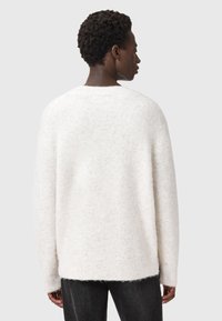 Suéter blanco, esponjoso y de punto con un corte holgado, hombros caídos y dobladillo acanalado. Textura suave con un diseño minimalista.