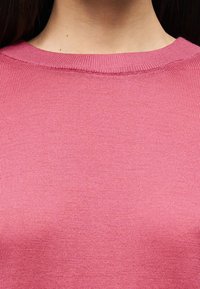 Ροζ ριμπ πλεκτό τοπ με στρογγυλή λαιμόκοψη, λεία υφή και διακριτικό οριζόντιο σχέδιο. Κοντινή λήψη που αναδεικνύει τις λεπτομέρειες κατασκευής.