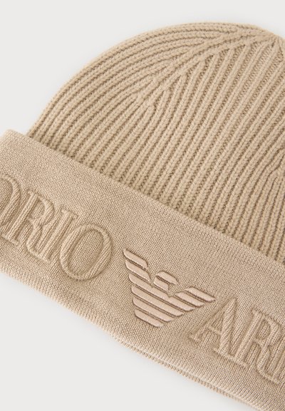 Bonnet en maille côtelée beige avec revers, présentant un texte en relief "Emporio Armani" et un logo aigle brodé.