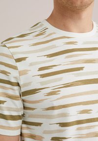 Tricou cu mânecă scurtă, în crem deschis, cu modele orizontale de pensulă în verde măsliniu și bej, având un guler rotund ribbat.