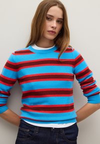 Maglione a righe con bande blu, rosse e marroni alternate, con collo e polsini a coste, indossato sopra una maglietta bianca.