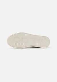Hvit sneaker såle, teksturert gummi med fiskebeinmønster og hevet skrift. Flat, bred form, designet for grep og stabilitet.